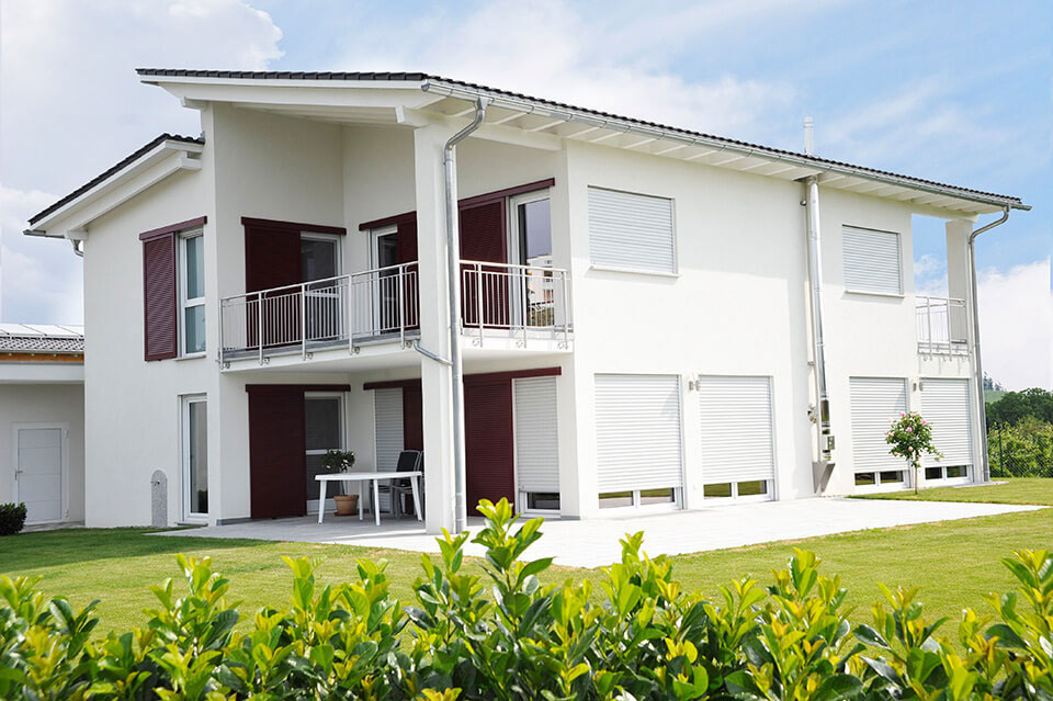 Detached house with white windows and roller shutters.